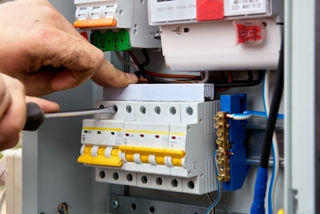 a hand holding a screw driving working on an electrical panel